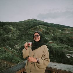 Portrait of beautiful young woman standing by mountains against sky