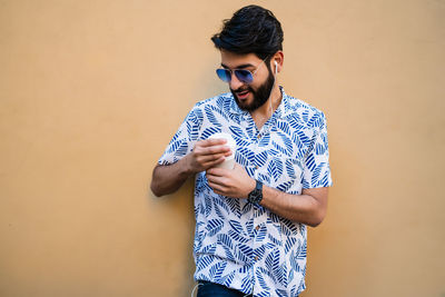 Young man wearing sunglasses standing against wall outdoors