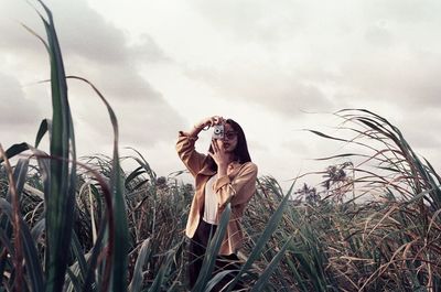 Woman standing by plants on field against sky