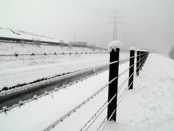 Snow covered barbed wire on field against sky