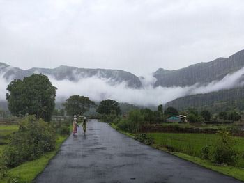 People walking on road against sky during rainy season
