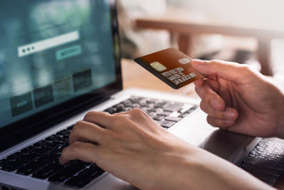 Cropped image of hands using credit card and laptop