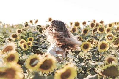 Rear view of woman on sunflower field against sky