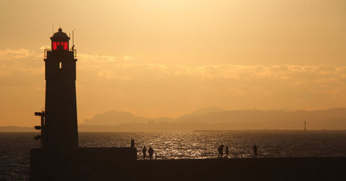 Silhouette lighthouse by sea against sky during sunset