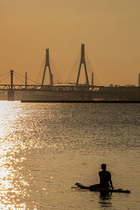 Silhouette people in sea against sky during sunset