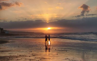 People standing on beach against sky during sunset