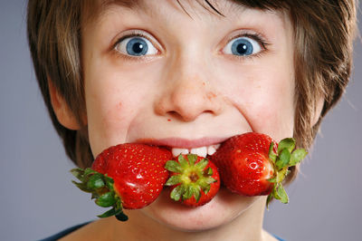 Close-up portrait of boy eating strawberries against wall