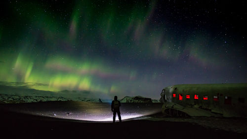 Silhouette man looking at aurora borealis while standing by abandoned airplane