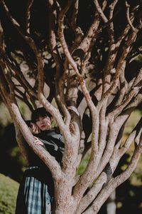 Portrait of young woman standing by tree at park