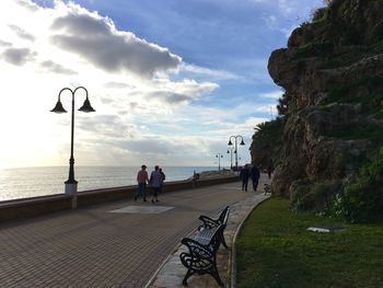 Rear view of people walking on promenade by sea