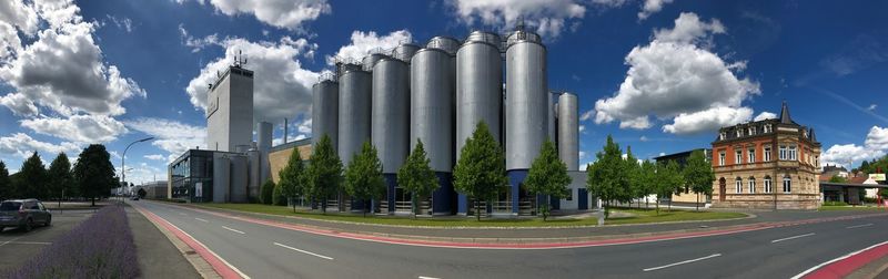 Panoramic view of road and factory against cloudy sky