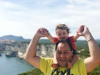 Portrait of happy father carrying son on shoulders at cliff