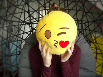 Woman covering face with anthropomorphic face cushion at home