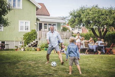 Father playing football with son while friends having fun at table in backyard party