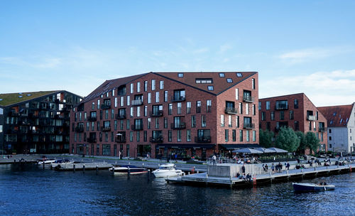 Sailboats moored on river by buildings against sky