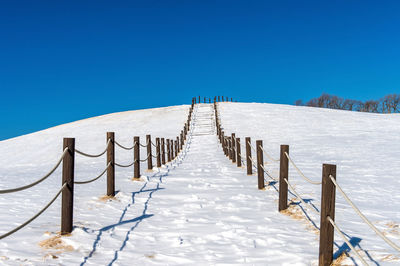 Wooden posts in snow against clear blue sky