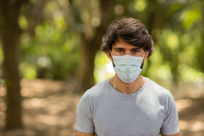 Handsome man wearing a medical protective mask on his face on a sunny day at park.