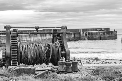 Abandoned metallic winch on beach against sky