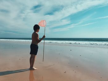 Full length of boy standing on beach against sky