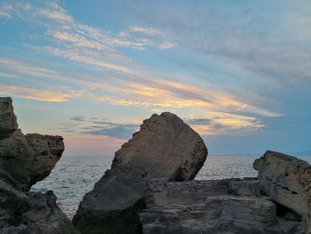 Rock formation on beach against sky during sunset