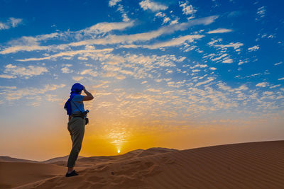 Man standing in desert against sky during sunset