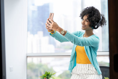 Smiling young woman using mobile phone in office against window