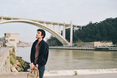 Young woman standing on bridge over river against sky