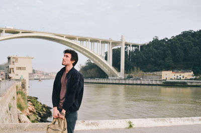 Man looking away while standing against bridge