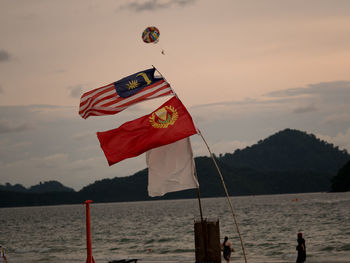 Flags on pole by sea against sky during sunset