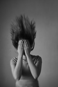 Woman with face hiding with hands standing against wall