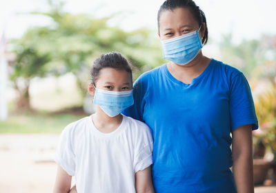 Portrait of mother and daughter wearing masks while standing outdoors