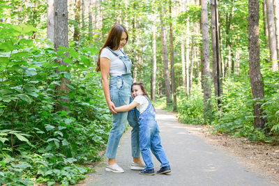 Full length of mother and daughter standing by tree