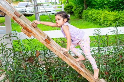 Full length of girl climbing on wooden plant at park
