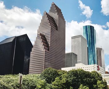 Low angle view of modern buildings against cloudy sky during sunny day