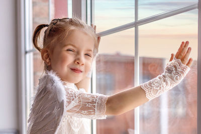 Portrait of young woman with arms crossed standing against window