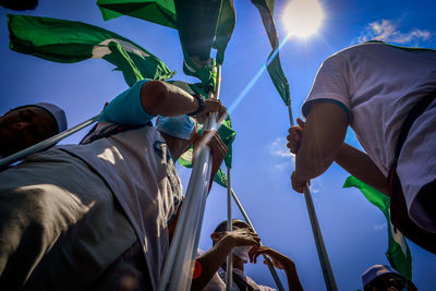 Low angle view of men holding flags against blue sky during sunny day