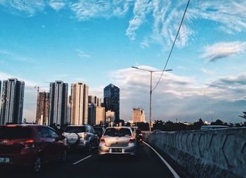 Cars on city street against sky during sunset