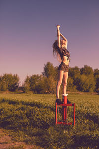 Young woman standing on equipment over field against sky during sunset