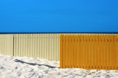 Scenic view of sandy beach with wooden fences against clear blue sky