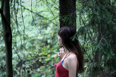 Side view of young woman standing in forest