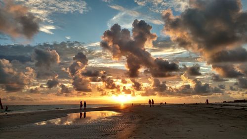 Silhouette of people at beach against cloudy sky