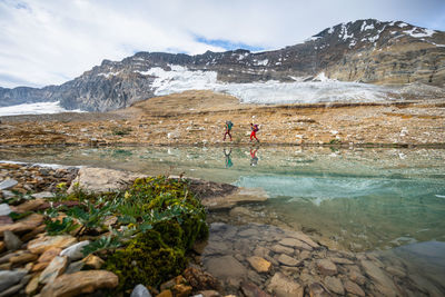 Backpackers hiking alongside alpine lake near a glacier in yoho