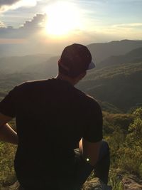 Rear view of man sitting on landscape against sunset sky