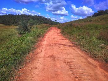 Dirt road amidst field against sky