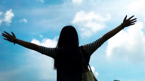Low angle view of woman with arms outstretched against sky