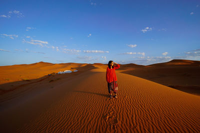 Rear view of man on sand dune in desert against sky