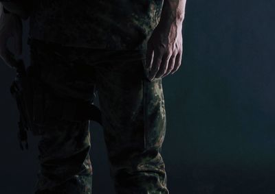 Midsection of army soldier standing against black background
