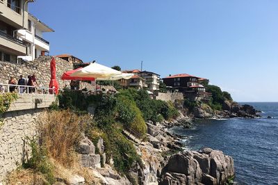 Plants and buildings by sea against clear sky