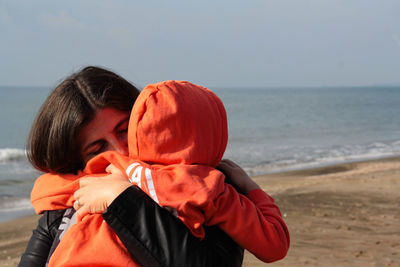 Rear view of mother and daughter at beach against sky