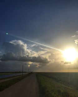 Road amidst field against sky during sunset